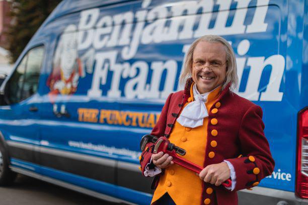 Benjamin Franklin mascot smiling in front of Benjamin Franklin Plumbing work van