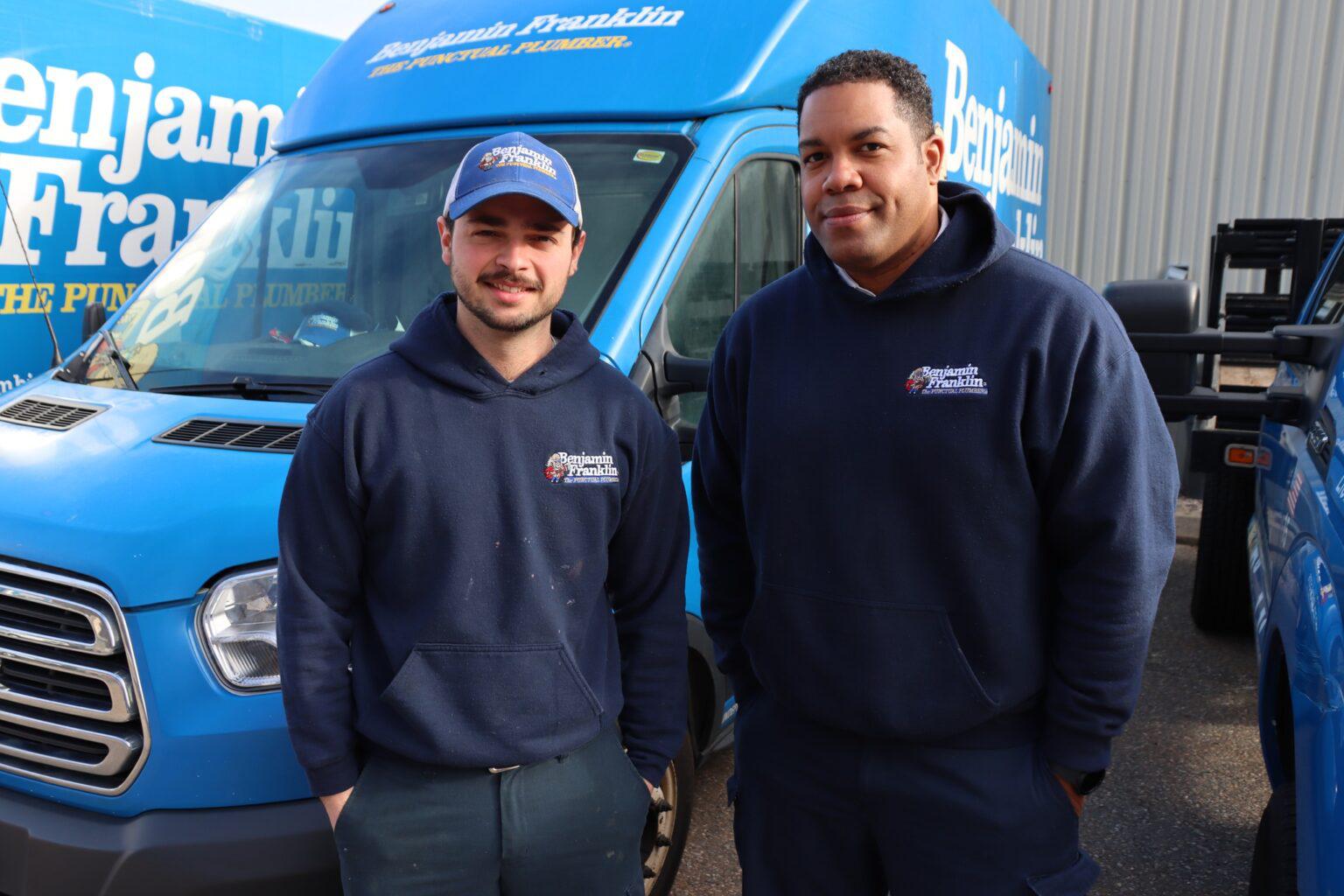 Two men smiling in front of Benjamin Franklin Plumbing work van